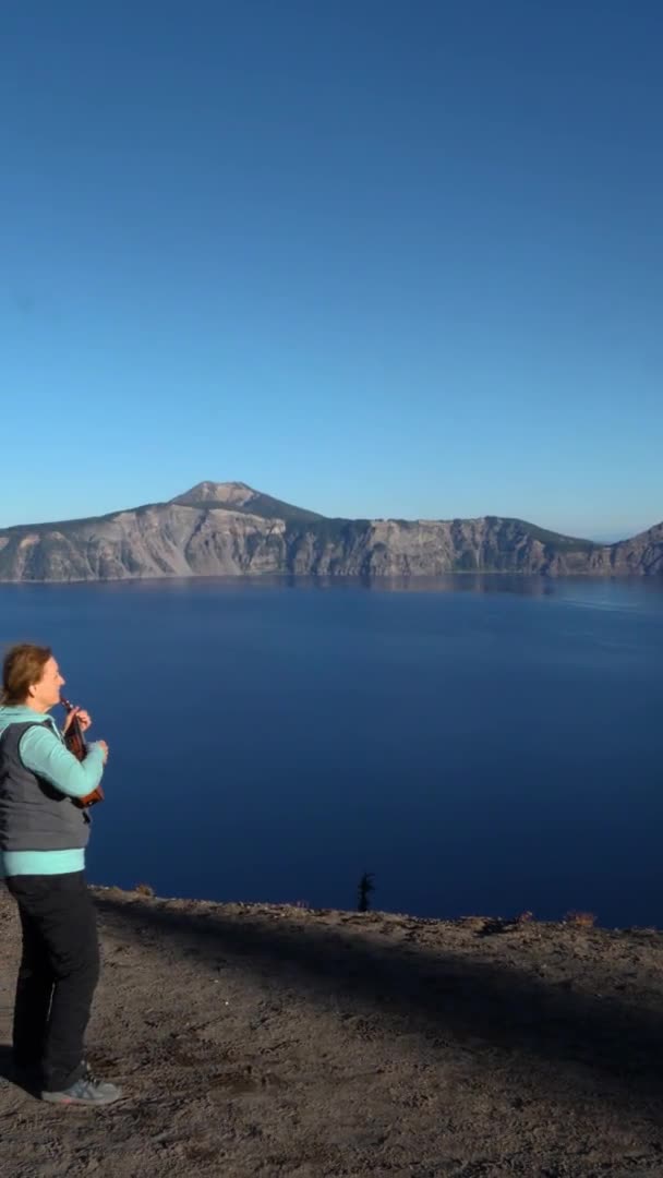 一个红头发的女人在火山湖国家公园的顶上弹奏她的四弦琴 — 图库视频影像