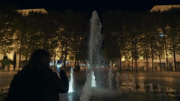 少女は夜公園で小さな噴水を撮影しています — ストック動画