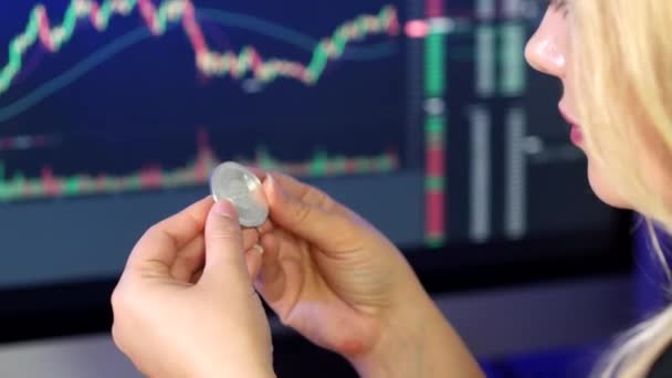金发女人手里拿着并看着藏在加密货币交易图前的卡达诺硬币 — 图库视频影像