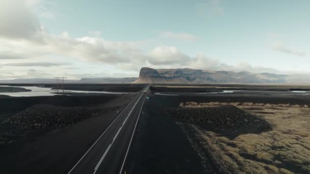 アイスランドの黒い火山砂砂漠を通って高速道路の橋を運転車の空中フォロー — ストック動画