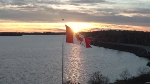 Aerial Push Bandeira Canadense Voando Durante Pôr Sol Sobre Água — Vídeo de Stock