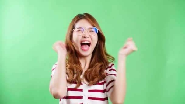 亚洲年轻女子举着眼镜在工作室的绿色背景上欢庆 — 图库视频影像