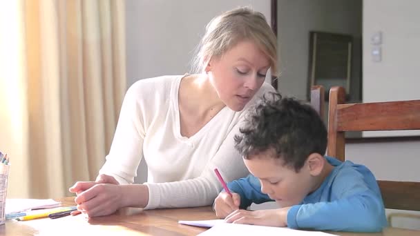 boy doing homework learning at home with mother with child sitting at a table stock video