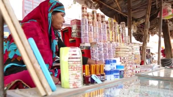 여자가 인도의 마을의 가게에서 액세서리와 장난감을 손으로 — 비디오