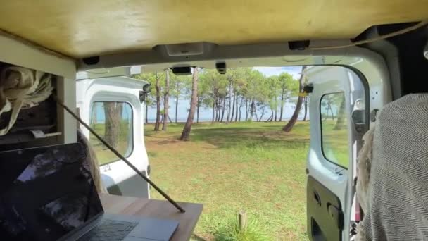 仕事と旅行 ドアが開かれたバンの内側からの眺め 海や湖の前の旅行中にラップトップを使用してください ヴァン コンバージョン — ストック動画