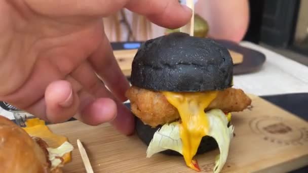 Hand Grabs Black chutné Mini Burger s rybami. POV Shot of Guy jíst malý burger s tekutým sýrem v restauraci.