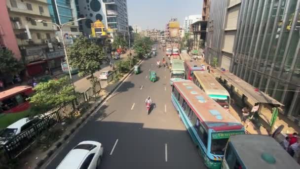 在达卡繁忙的道路上 在阳光灿烂的日子里 乘坐公共汽车和汽车开着车 从人行道上倾斜向上看 — 图库视频影像