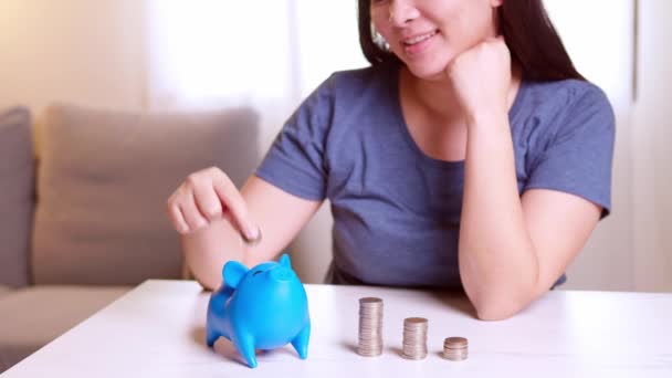 Stack of coins with a young woman putting coins into the blue piggy bank. Saving money for future investment concept.