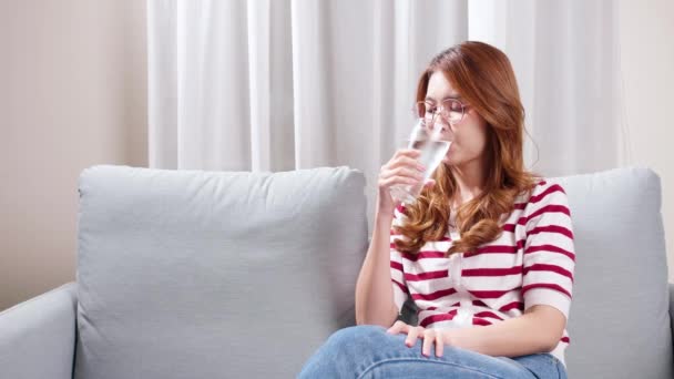 亚洲年轻女子坐在沙发上喝水 以缓解严重头痛 — 图库视频影像