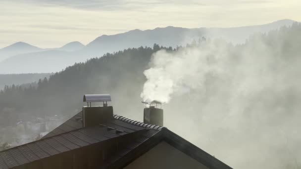 冬に煙突から煙が立ち上る 冬に暖房のために木を燃やしている間 白い煙は煙突から来ています 背景にある山 — ストック動画