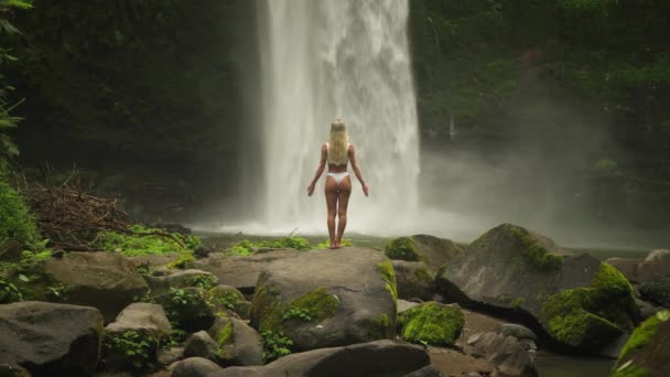 Nő fehér bikini felemeli karját köszönti erős patak vízesés, Nungnung