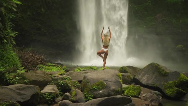 Mujer Rubia Árbol Yoga Pose Balance Con Potente Cascada Nungnung — Vídeos de Stock