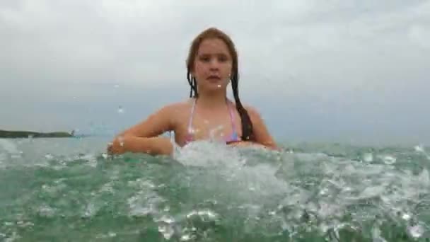ゆっくりと美しい笑みを浮かべて赤毛の小さな女の子のカメラに向けて海の水をはねの動き 低角度海水準のPov — ストック動画
