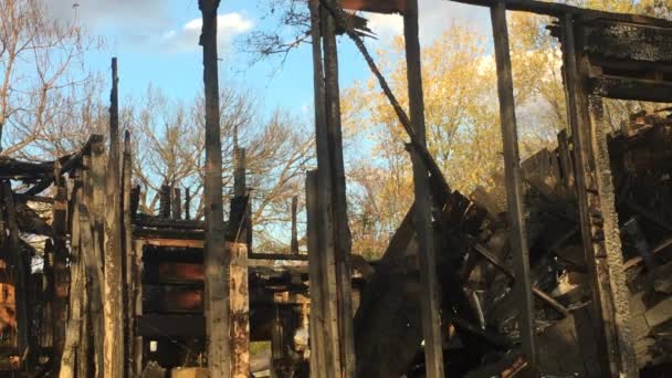 破壊的な家の火災の後に残る木製のフレーミングのアップショット 背の高い木に青い空が並んでいる家族の家の焼け跡に対して — ストック動画