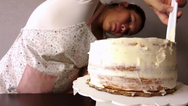 Latin nő visel kötényt készül főzés sütés egy torta terjed vaj cukormáz egy fehér műanyag torta spatula