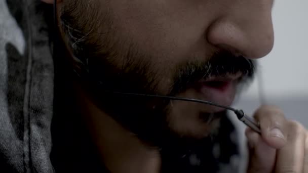 Közelkép egy szakállas indiai férfi arcáról, aki egy mikrofont tart egy fejhallgatóból a szája előtt, és nyugodtan beszél a hívóval a mobilján.