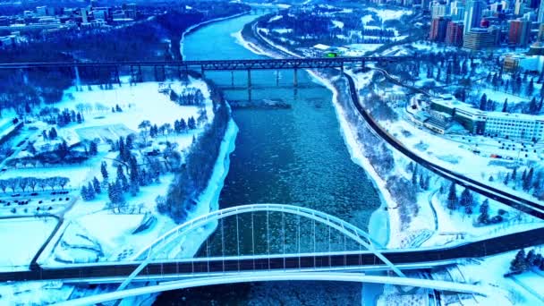 4K冬季空中留鸟俯瞰沃尔特 戴尔桥 冰片沿着萨斯喀彻温省北部河流流下 古老的高层大桥在地平线上 而冰雪覆盖着两个公园1 — 图库视频影像