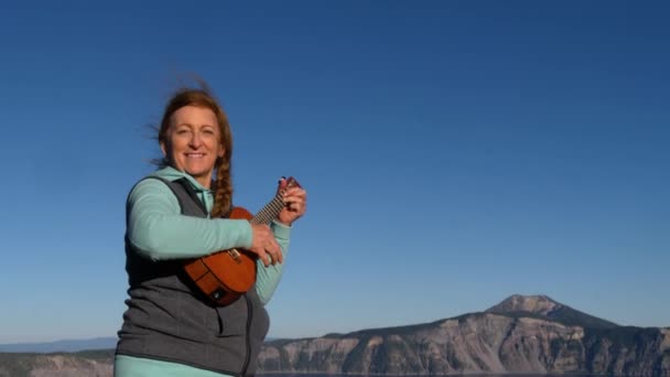 Een Vrouw Glimlacht Als Speelt Haar Ukelele Met Bergen Achter — Stockvideo