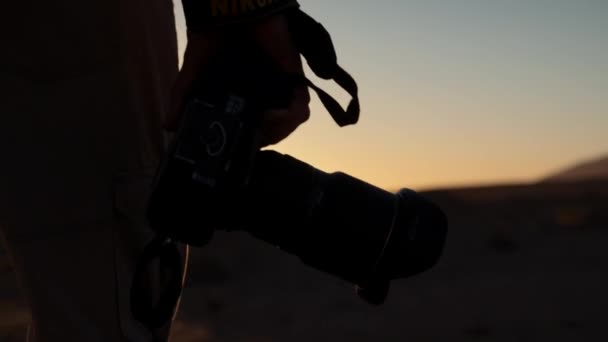 在非洲沙漠里 一个摄影师手拿着相机 朝着日落的方向走去 这是他拍摄的一个戏剧性的跟踪镜头 — 图库视频影像