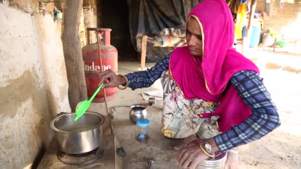 インドのラジャスタン州の農村部のポットとガスストーブの炊飯器で地面にお茶を準備貧しいインドの女性 手持ち — ストック動画