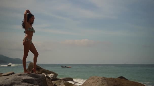 美丽的年轻女子穿着比基尼躺在岩石沙滩上 舒展在阳光下 慢动作 — 图库视频影像
