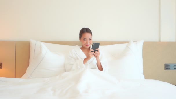 Krásná asijská žena kontrola zpráv na Smartphone v posteli na jasné ráno. Celý rámec