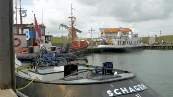 テクセルの港で古典的なボートの着実なショット 客船の隣には美しいタグボートと古いコースターがあります 背景には 虹の旗を持つ古いオランダの風車が見えます — ストック動画