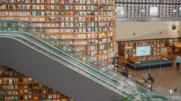 Návštěvníci používající eskalátor mezi patry v knihovně Starfield s obrovskými knihovnami na pozadí - panning timelapse shot 4k