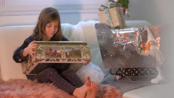 Meglepett és izgatott fiatal lány nyitó doboz ajándékokkal előtt karácsonyi dekoráció ajándékokkal és csomagokkal télapó szánkó. Széles lövés a boldog gyerek forgatott Pro Res 4K.