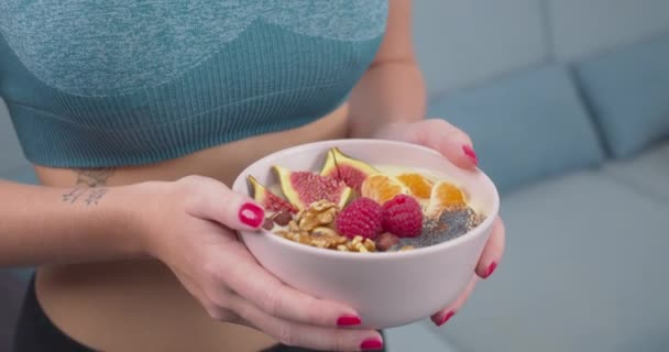 4K特写一个扁平的金发健康女人穿着运动服 早餐拿着一碗健康的水果和坚果 健康饮食 健身和健身的概念 — 图库视频影像