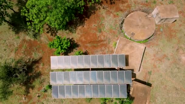 アフリカの農村部で太陽光で発電された水タンクです そうだ 4K太陽光パネルファーム 太陽電池 の空中ビュー 太陽光パネルフィールド上のドローン飛行再生可能な緑の代替エネルギー — ストック動画