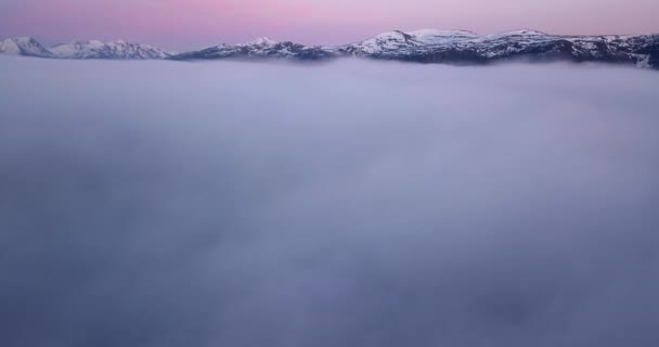 背景に絵のように美しい雪の山と日没後の低レベルの雲の毛布の上に蛇行し 前方の飛行ハイパーラプス ゆっくりと雲の中に降りていく — ストック動画