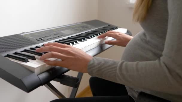 Těhotná žena střední dospělé hraje hudbu na syntezátoru pro dítě v břiše