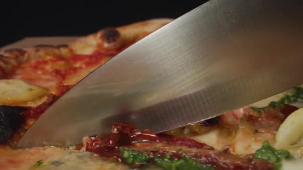 Zblízka záběr pizzy na stole. Lesklý nůž pomalu krájí pizzu..