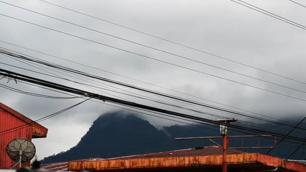 快速移动的云朵的时间流逝低垂在阿基里火山和塞罗脉冲星之上 锈迹斑斑的铁皮屋顶和电缆在前景而漆黑的天空在背景中飞驰而过 哥斯达黎加拉福尔图纳全市 — 图库视频影像