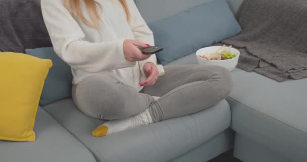 若いです女性オンソファオンテレビ箸でポークボウルを食べながら — ストック動画