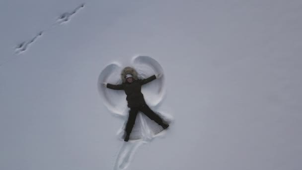 深い雪の上に横たわっているフィンランドの若い女の子の上に空中雪の天使を作る ズームアウト — ストック動画
