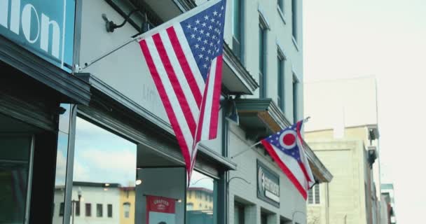 在一个古色古香的小镇的人行道上 美国和俄亥俄州的国旗在一家小商行前面摇曳着 以4K慢动作射击 — 图库视频影像