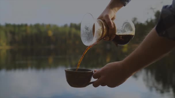 ガラス製のコーヒーメーカーを注ぎ 湖の森の背景にカップにカフェインを注ぐカフェテリア — ストック動画