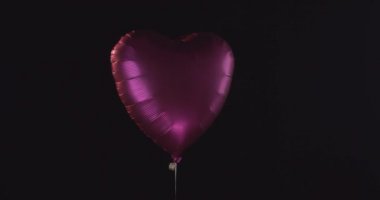 Pembe renk kalp şekilli balon. Düşen kalpler siyah arka planda izole edilmiş.