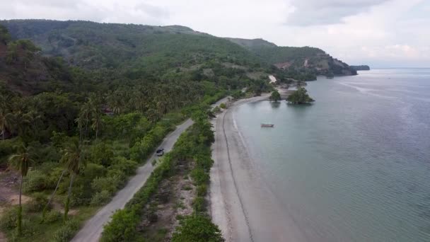 熱帯アトーロ島 東チモール 東南アジアの木々や海に囲まれたでこぼこ砂利道に沿って移動するトラックの上昇空中ドローン — ストック動画