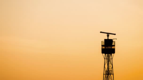 夕日の空の下で回転アンテナを備えたシーレーダータワーのシルエット — ストック動画