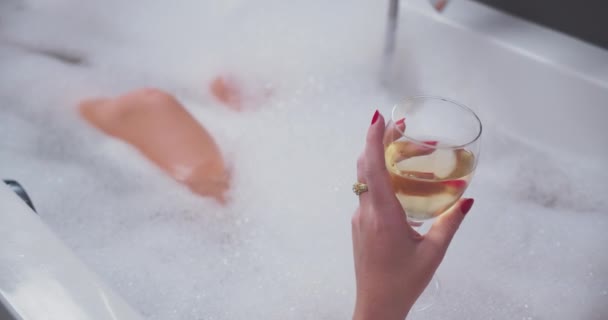 Zavřít na bublinkovou koupel a dívka pije sklenici vína při relaxaci.