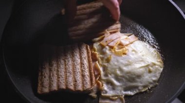 Jambon ve erimiş peynirle kaplanmış kızarmış bir yumurtanın yanına yakın plan bir tost ekmeği yerleştirilir. Dolgu ekmeğin üzerine konur ve sandviçin montajını tamamlar.
