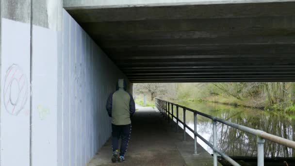 Tył Anonimowego Człowieka Idącego Pod Mostem Ścieżka Biegnąca Równolegle Brzegu — Wideo stockowe