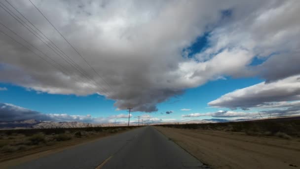 在阴云密布的日子开车沿着空旷的莫哈韦沙漠公路行驶 两旁有电线杆 远处有山 司机的观点 — 图库视频影像