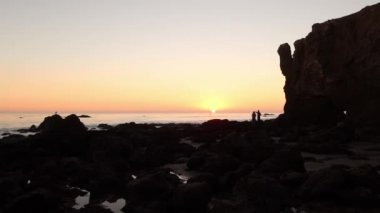 Kaliforniya 'daki El Matador plajında dalgalarla gün batımına bakan bir çiftin romantik anı.