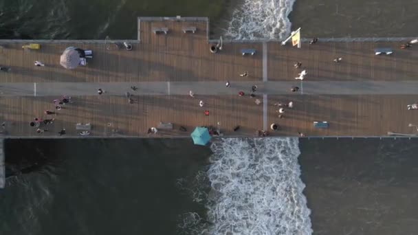 サンタモニカの桟橋を歩く人々と波がビーチの空中風景に押し入る — ストック動画