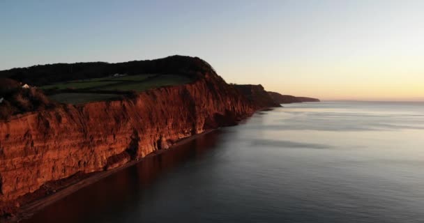 ジュラシック コーストの赤い崖の空中前方ショット美しい穏やかな海と日の出で南西イングランド — ストック動画