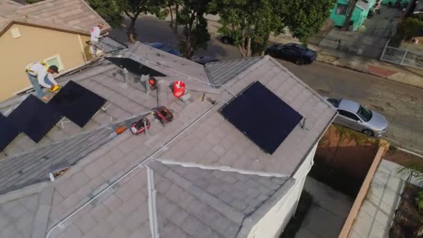 労働者たちは 晴れた日にカリフォルニア州ロサンゼルスの現代的な家の屋根の上にソーラーパネルを設置することに忙しい 空中ドローン — ストック動画